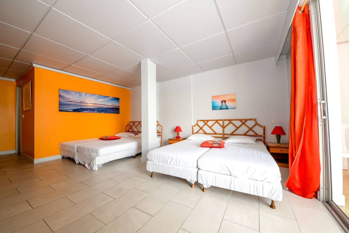 A hotel room with two beds, a painting on the wall, and a window with orange curtains.