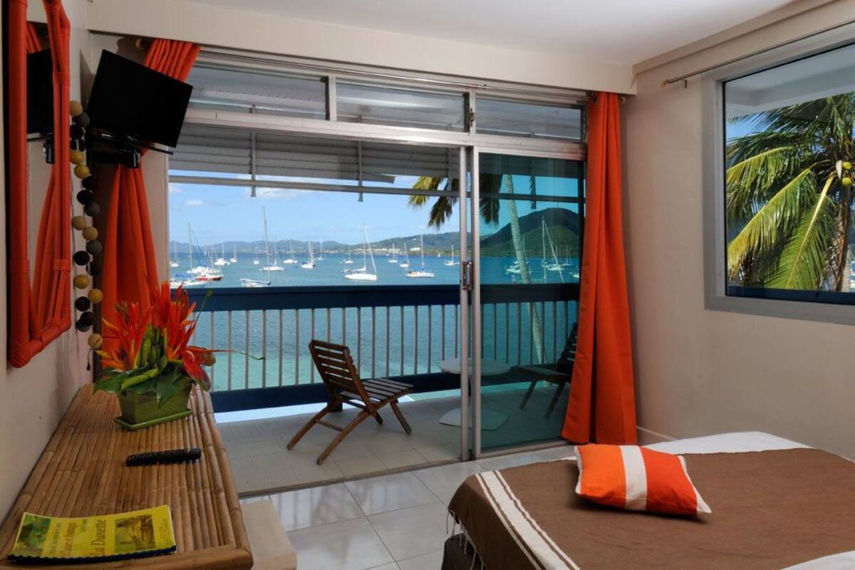 A hotel room with a balcony, a bed, a chair, a table, and a TV.