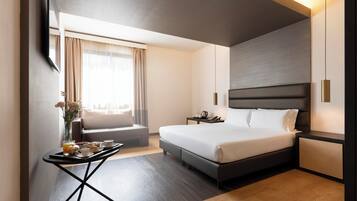 Una habitación de hotel moderna con una cama grande, mesitas de noche, una pequeña zona de estar y una bandeja de desayuno.