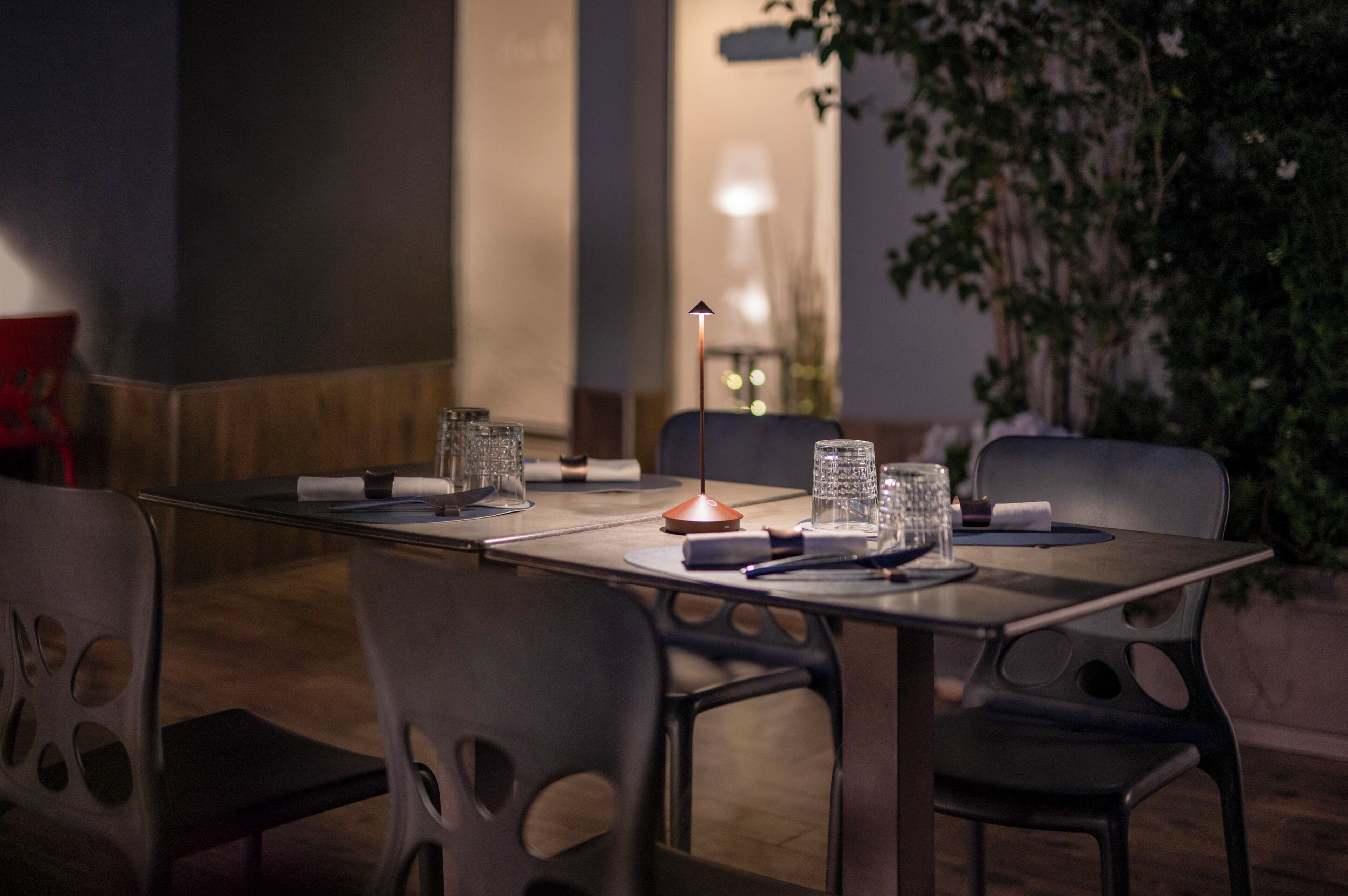 An outdoor dining area with a table set for two, surrounded by chairs, and a lamp in the background.