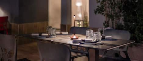 Un área de comedor al aire libre con una mesa dispuesta para dos personas, rodeada de sillas y una lámpara al fondo.