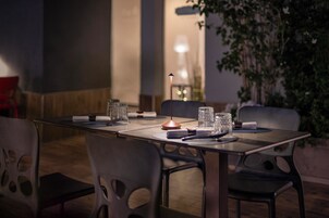 An outdoor dining area with a table set for two, surrounded by chairs, and a lamp in the background.