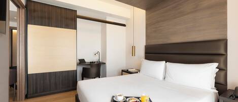 A hotel room with a bed, bedside table, and a tray with breakfast items.
