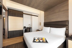 Una habitación de hotel con cama, mesita de noche y bandeja con productos para el desayuno.