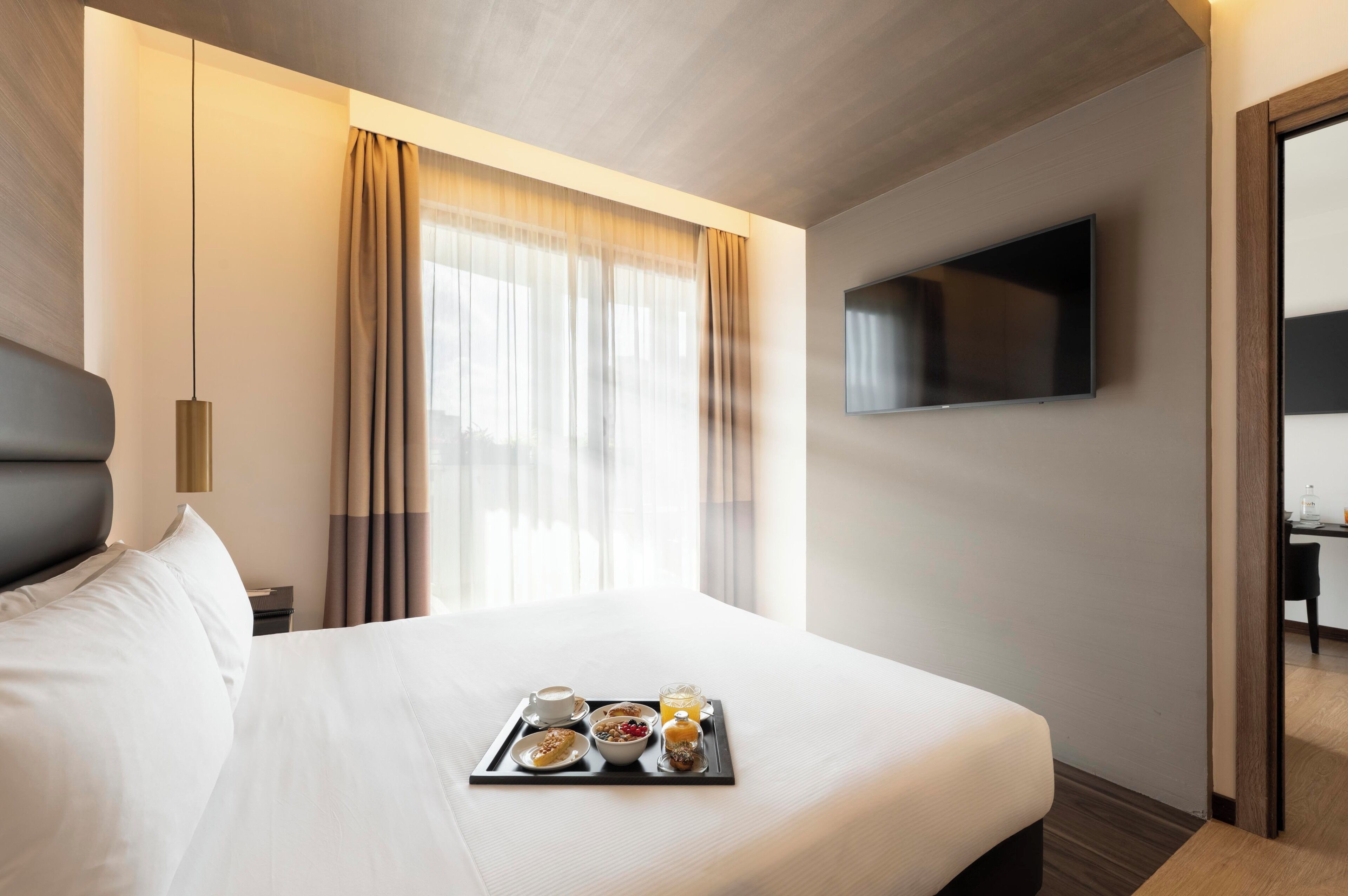 Una camera d'albergo con un letto, un vassoio con prodotti per la colazione, una televisione e una finestra con tende.