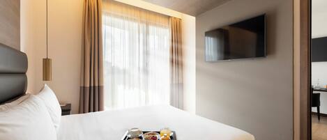 Habitación de hotel con cama, bandeja de desayuno, televisor y ventana con cortinas.