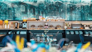 Un bar à petit-déjeuner moderne, agrémenté d’une fresque représentant un paysage urbain, d’un buffet proposant des viennoiseries et d’un espace dédié au café.