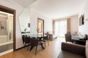 A modern hotel room with a dining area, a sofa, a TV, and a large mirror.