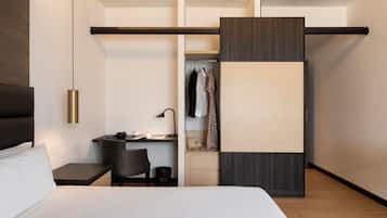 Quarto de hotel moderno com cama, escrivaninha, cadeira, guarda-roupa e cabideiro.