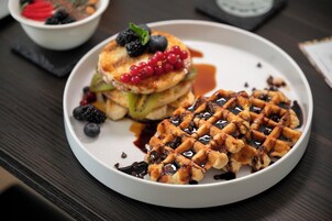 A plate of pancakes with berries and syrup, and a waffle with chocolate chips and syrup.