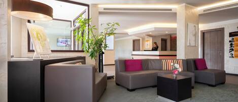 En moderne hotellobby med receptionsdisk, siddeområde og et stort vindue.