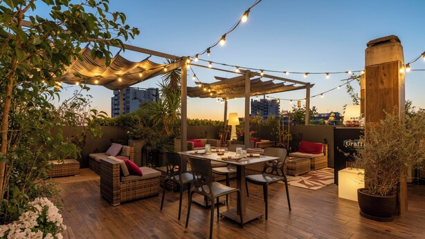 Une terrasse extérieure avec des meubles en osier, des guirlandes lumineuses et une pergola.