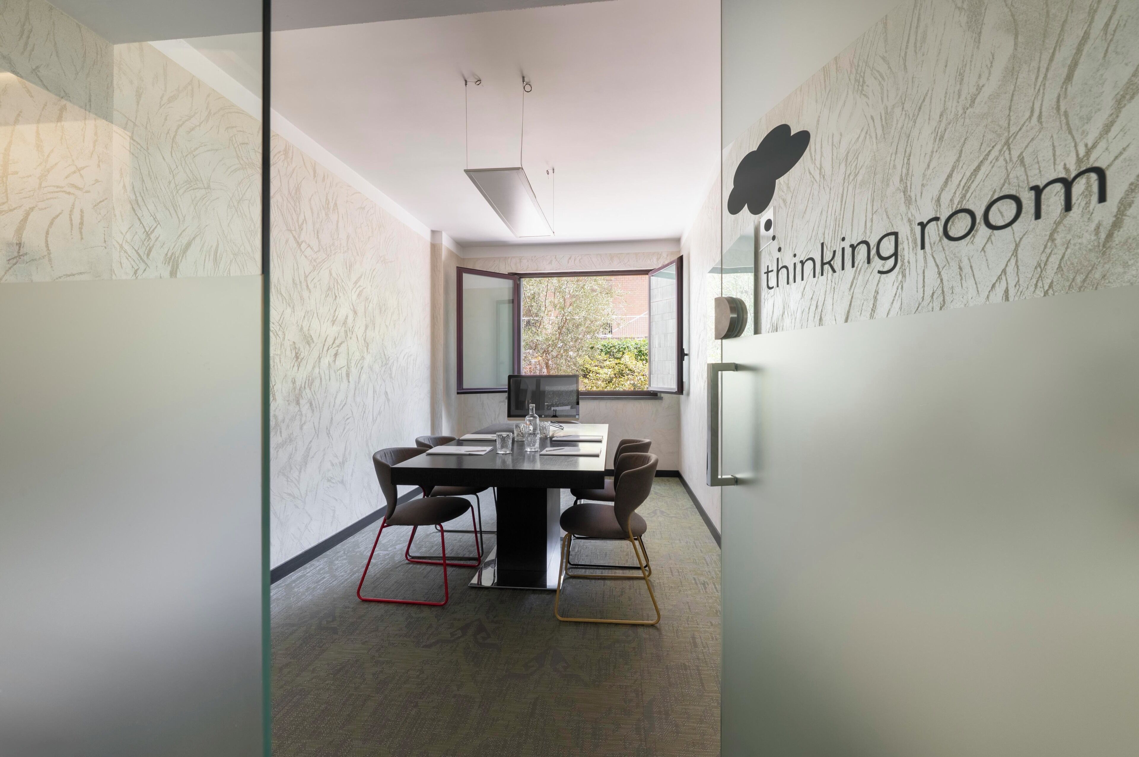 A modern conference room with a glass partition, a table with chairs, and a 'thinking room' sign on the wall.
