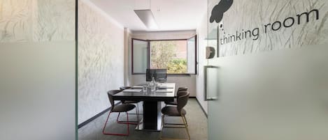 A modern conference room with a glass partition, a table with chairs, and a 'thinking room' sign on the wall.