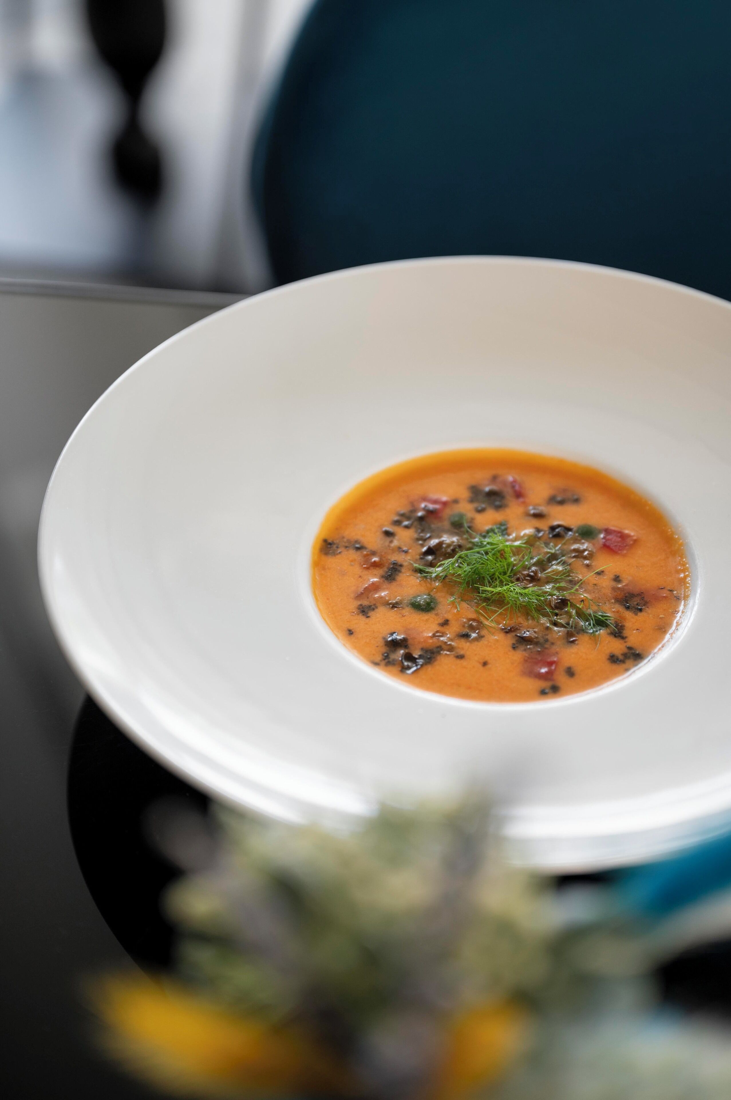 A white bowl of soup with herbs and a garnish on a table.