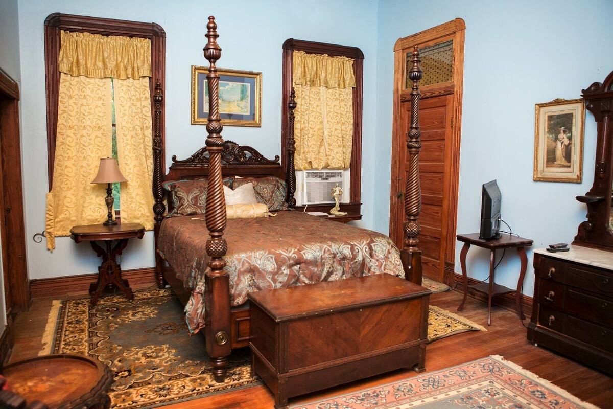 Un dormitorio tradicional con una cama con dosel, un baúl de madera, un escritorio con computadora y un aparador.