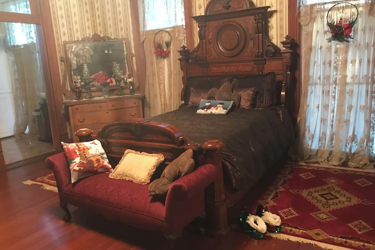 Un dormitorio tradicional con una cama y un aparador de madera, un espejo y un sillón rojo.
