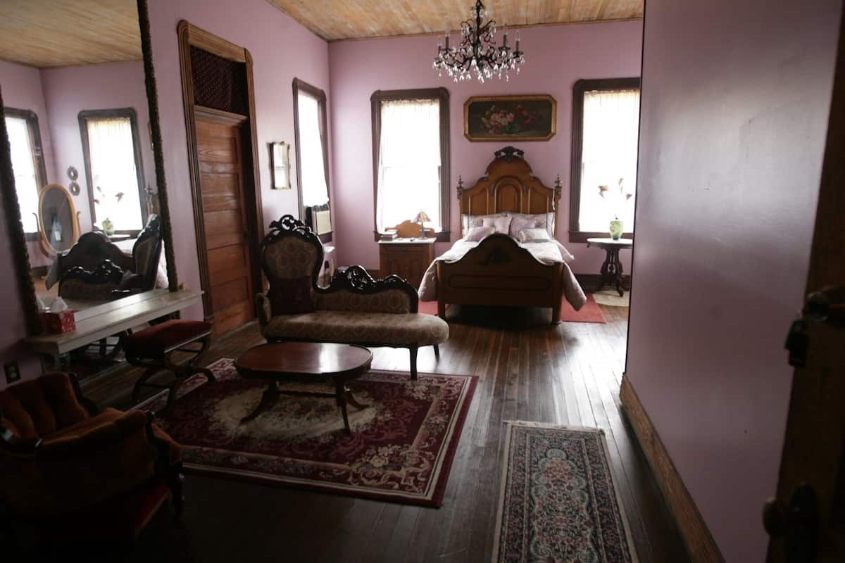 Un dormitorio con una cama de madera, una silla, una mesita y una araña.
