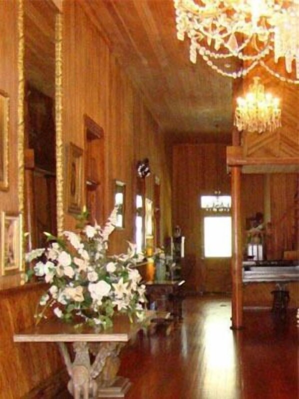A wooden interior with a chandelier, a table with flowers, and a window with natural light.