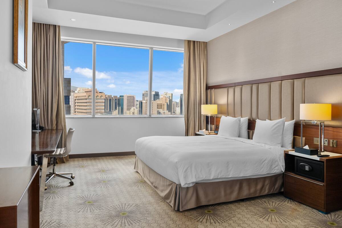 A hotel room with a large bed, two bedside lamps, a desk, and a chair.