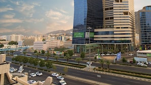 Um edifício moderno com fachada de vidro e uma mistura de estilos arquitetônicos, incluindo uma estrutura curva e um prédio retangular com linhas horizontais.