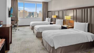 A hotel room with two beds, a desk, a TV, and a city view.
