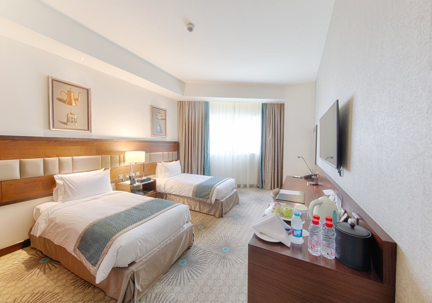 A hotel room with two beds, a desk, a television, and a window with curtains.