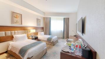 A hotel room with two beds, a desk, a television, and a window with curtains.