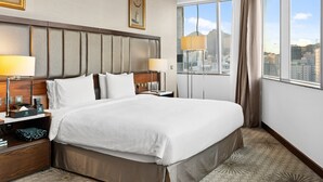 A hotel room with a large bed, two bedside tables, a nightstand, a large window with a city view, and a headboard with a decorative panel. - Makkah Al Aziziah (Makkah)