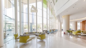 Um amplo hall de entrada com grandes janelas, área de estar central com sofás e poltronas, e uma moderna recepção.