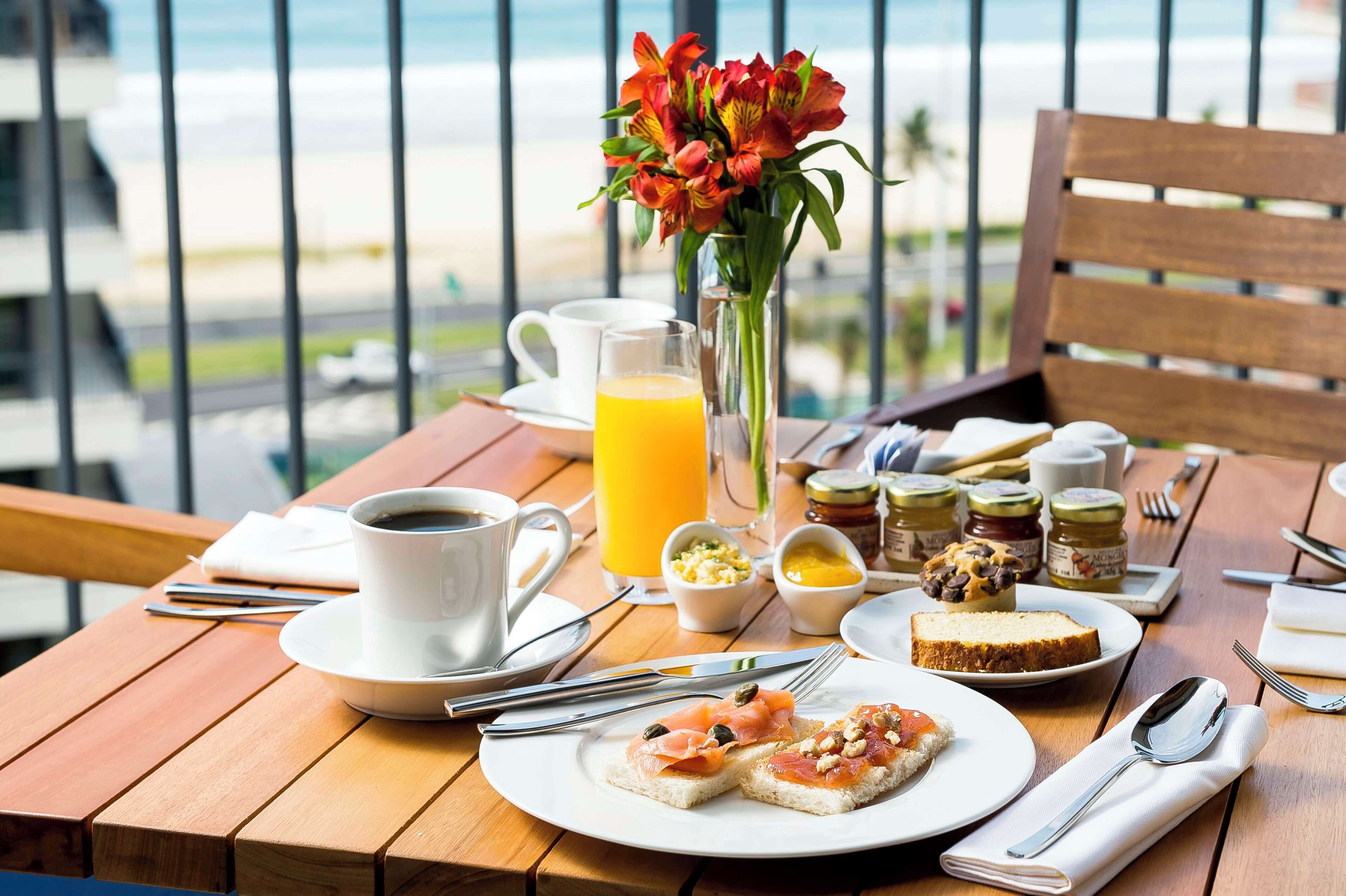 A breakfast table with a cup of coffee, a glass of orange juice, a vase of flowers, and a plate of toast with salmon and eggs.
