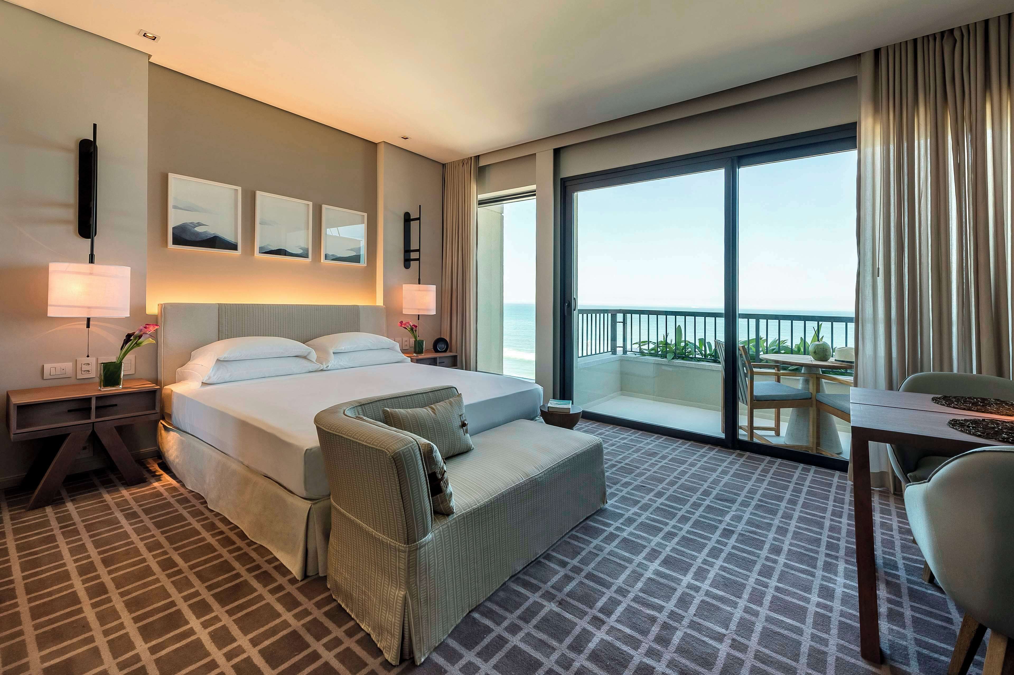 Habitación de hotel con una cama grande, un sofá, un escritorio y un balcón con vista al mar.