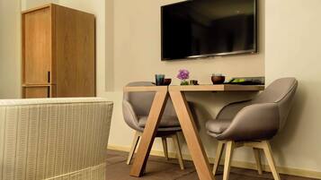 A modern room with a wooden cabinet, a TV mounted on the wall, a dining table with two chairs, and a small vase with flowers.