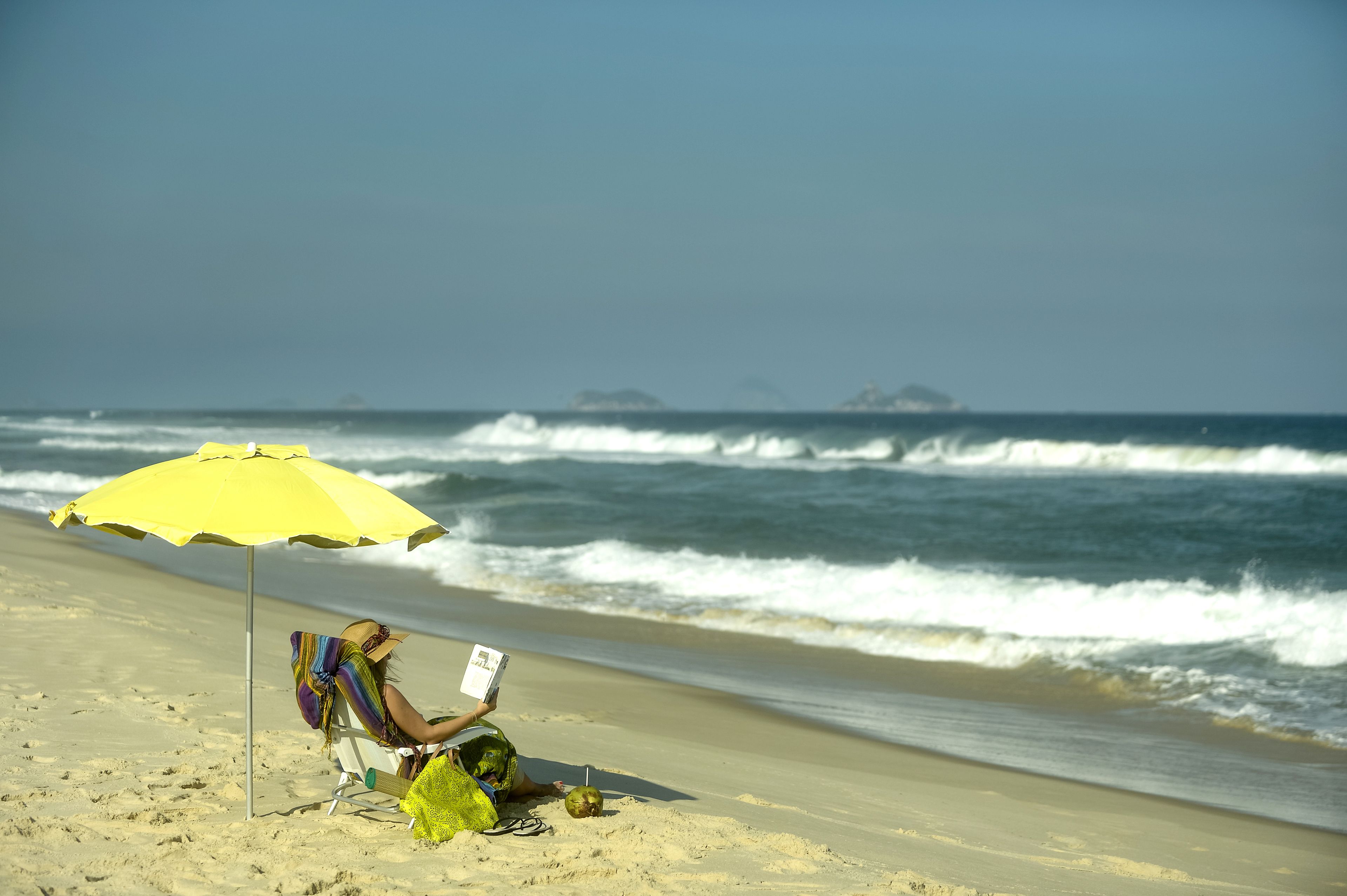A person sitting on a beach chair under a yellow umbrella, reading a book.