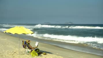 A person sitting on a beach chair under a yellow umbrella, reading a book.