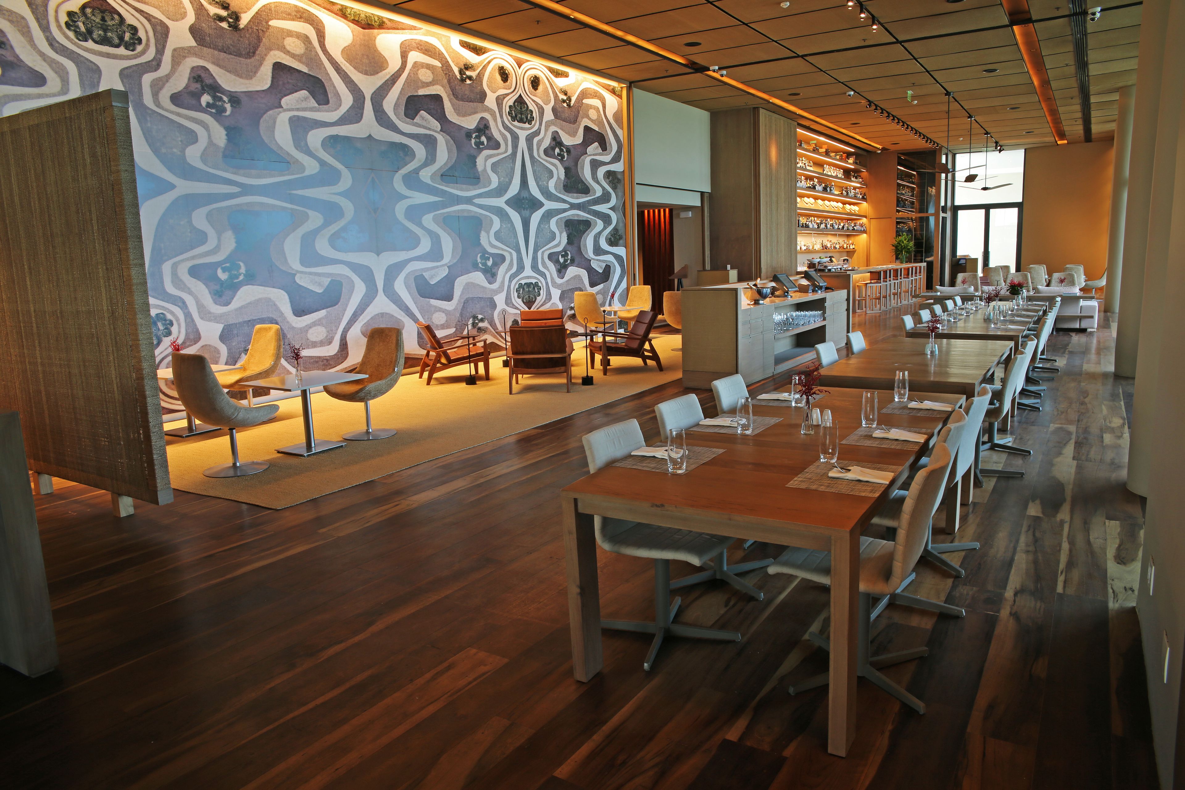 A modern restaurant with a long dining table, multiple chairs, and a patterned wall.
