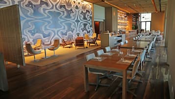 A modern restaurant with a long dining table, multiple chairs, and a patterned wall.