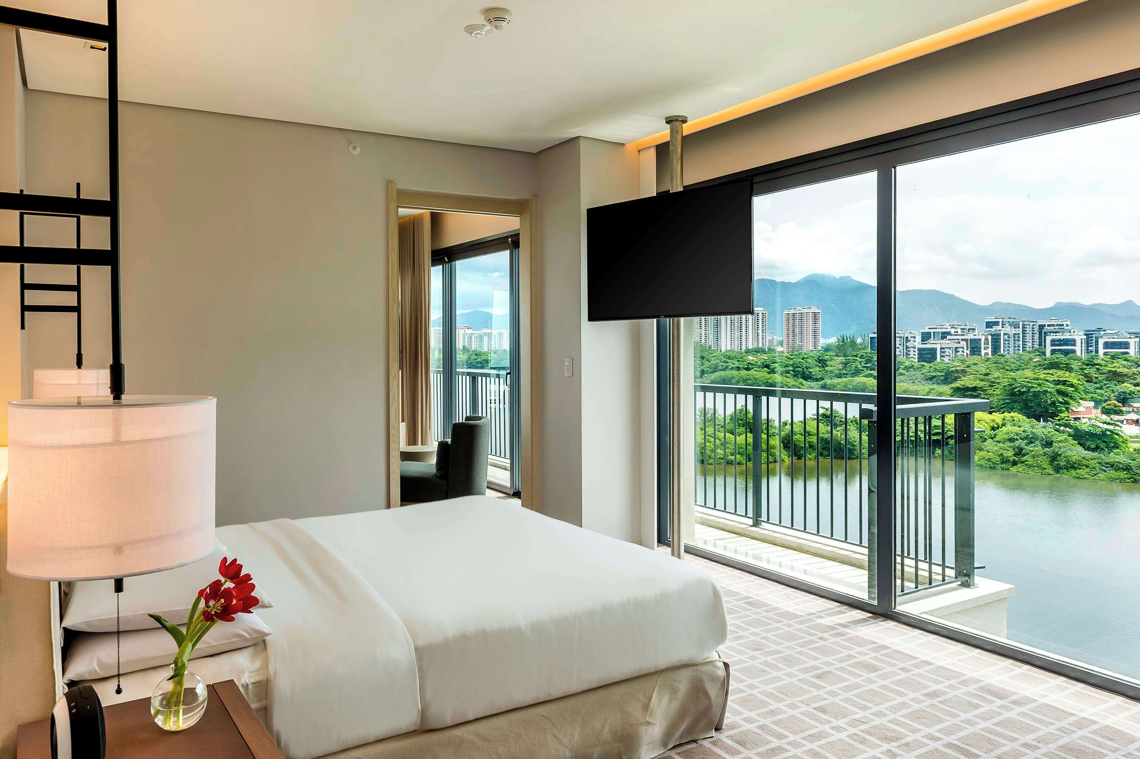 Quarto de hotel com cama, televisão, luminária e vista para o rio e a paisagem urbana.