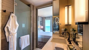 A modern hotel bathroom with a glass shower enclosure, a large mirror, a sink with a vanity, and a view of the sea through the adjacent bedroom. - Grand Hyatt Rio De Janeiro (Rio de Janeiro)