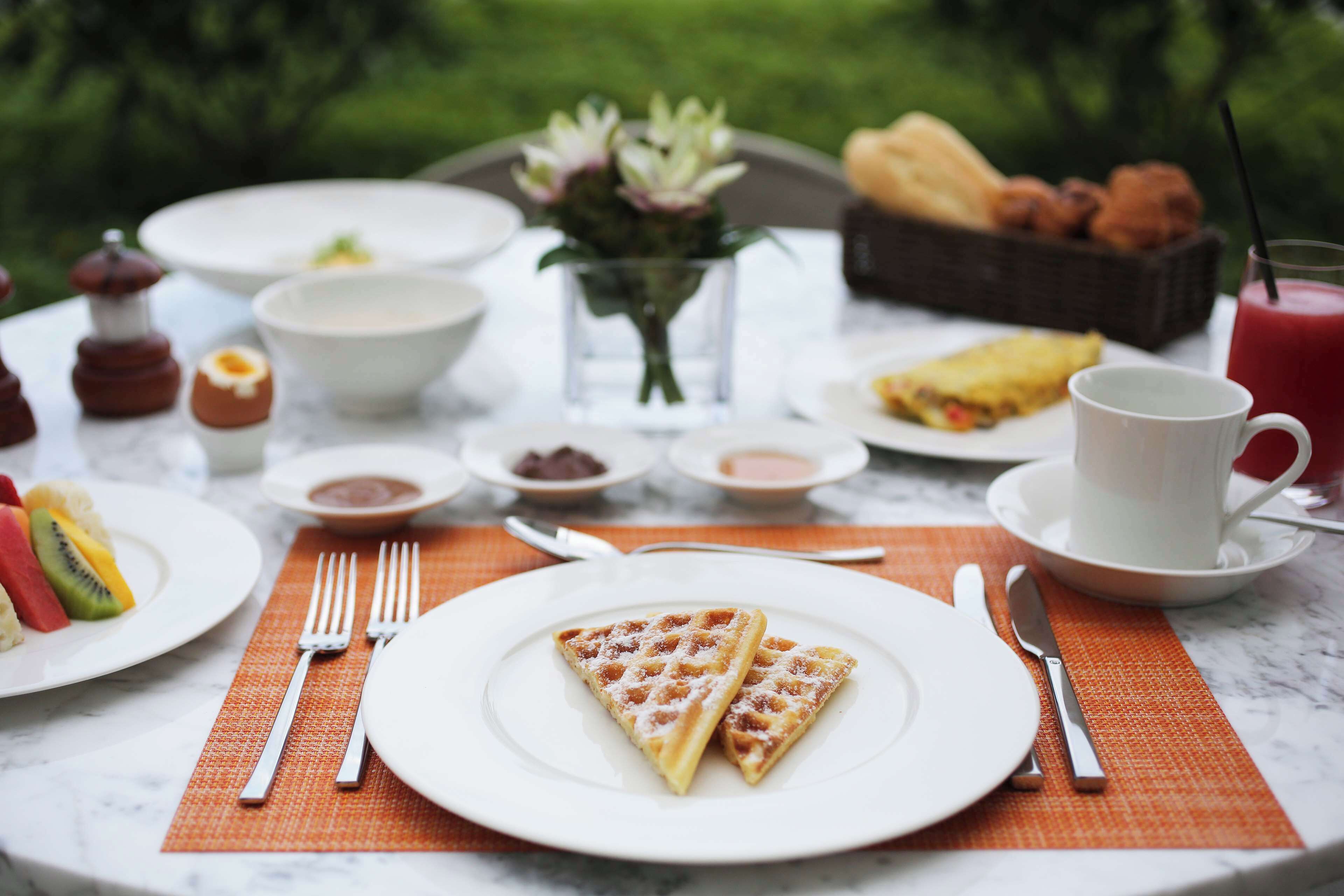 A breakfast setting with waffles, fruit, and a cup of coffee on a marble table.