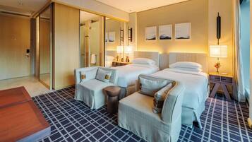 Habitación de hotel con dos camas, un sofá, una silla, una mesa de madera y una alfombra estampada.