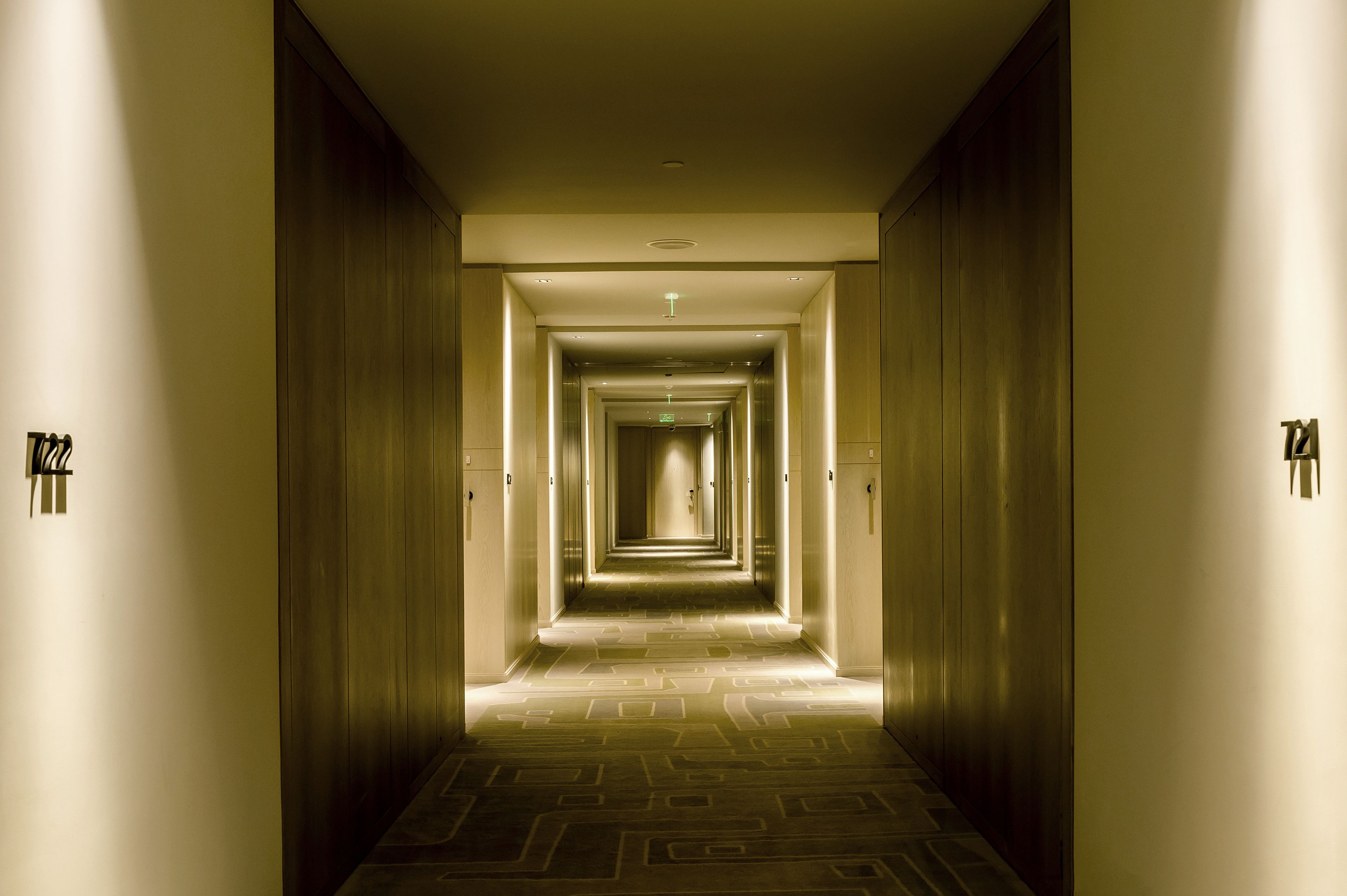 Un pasillo largo y estrecho en un hotel, con alfombra estampada e iluminación empotrada.
