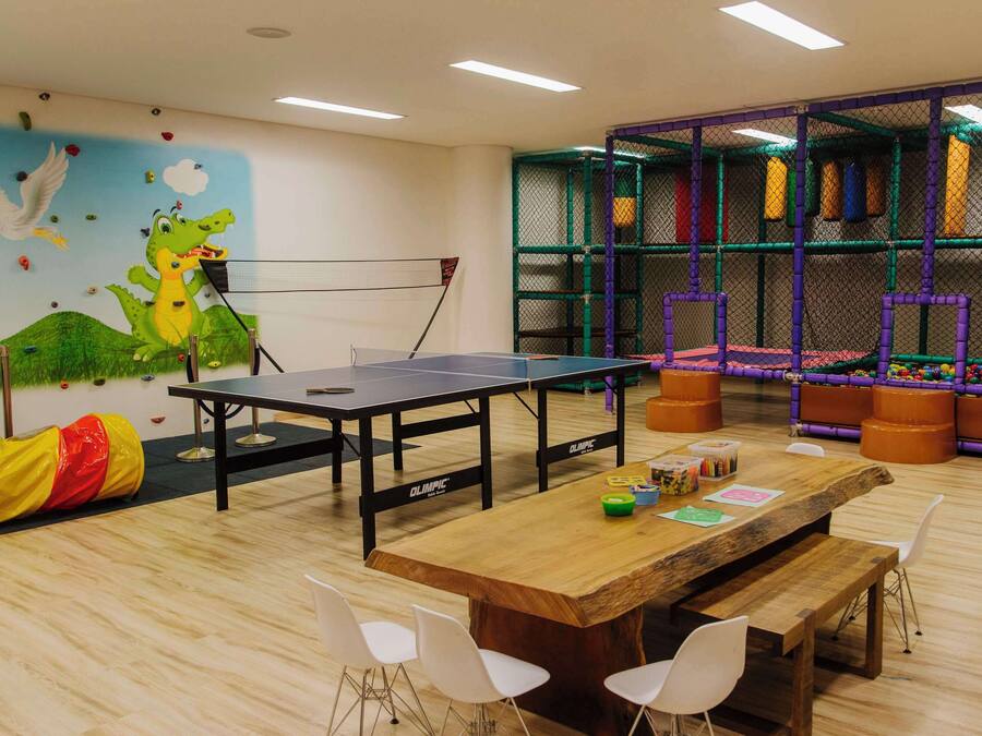Una habitación con mesas de ping pong, una mesa de madera con sillas, una pared de escalada y un mural colorido.
