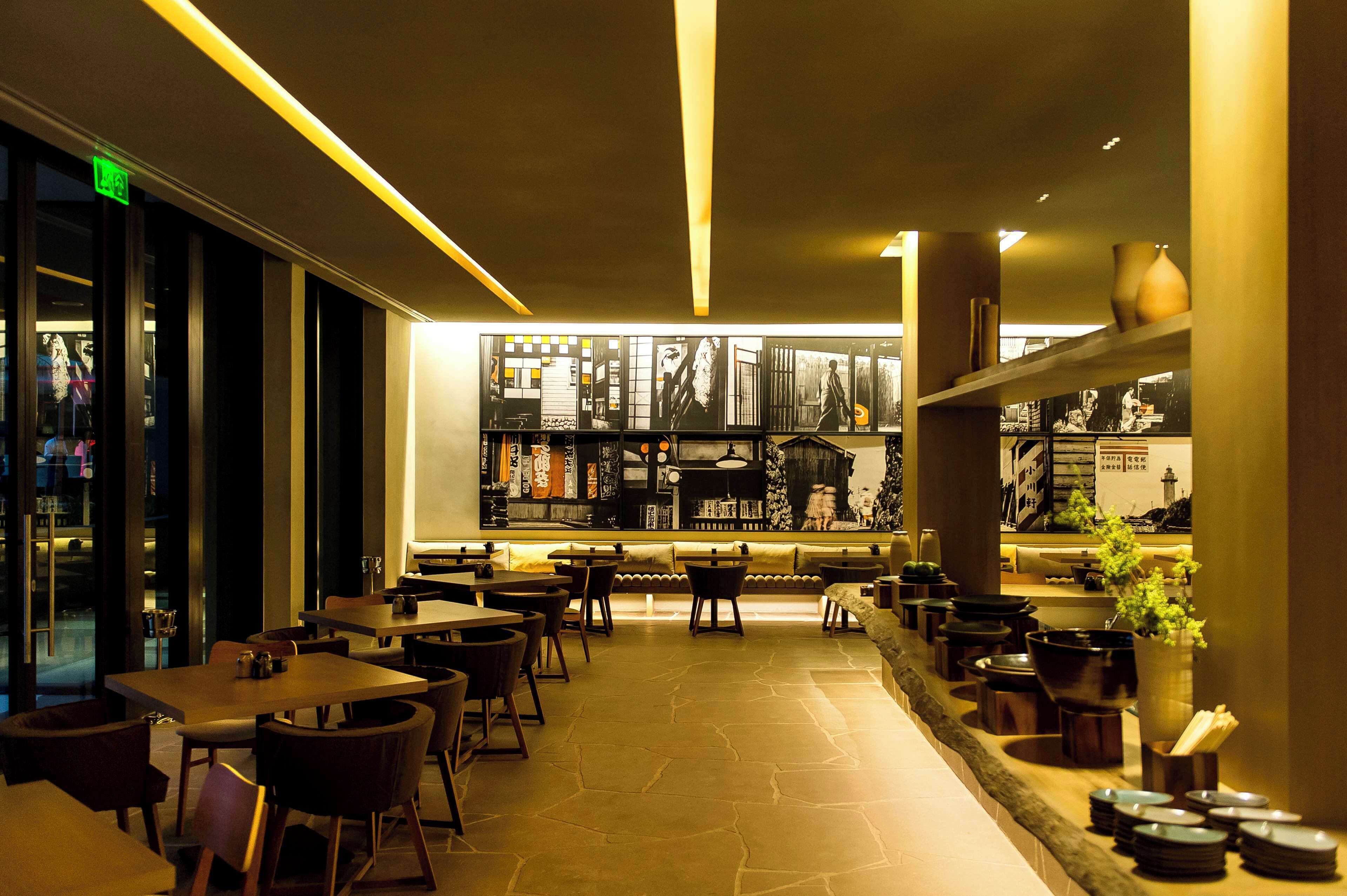 A restaurant with a long counter, tables, chairs, and a wall with framed pictures.