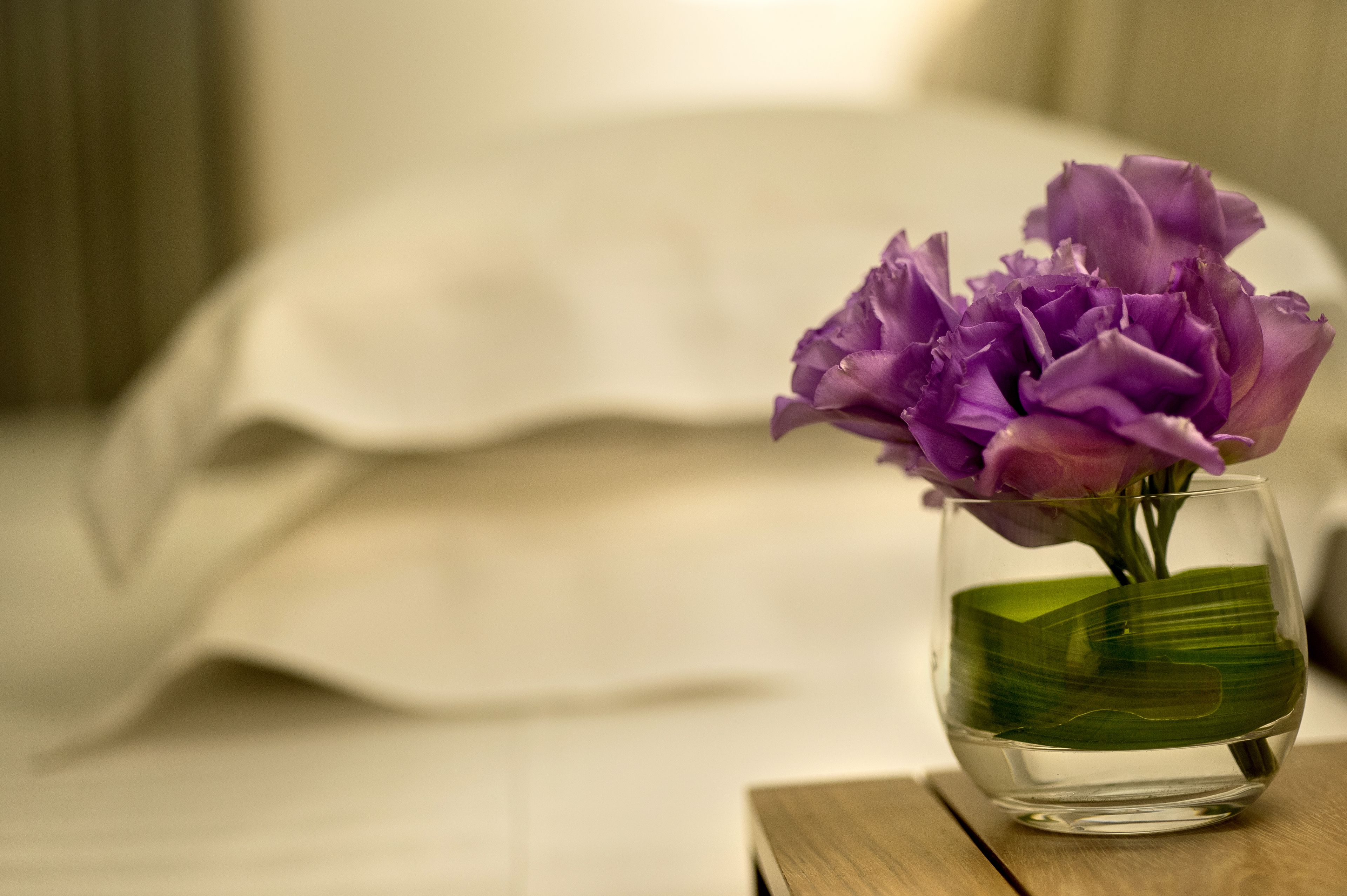A clear glass vase with purple flowers on a wooden table.