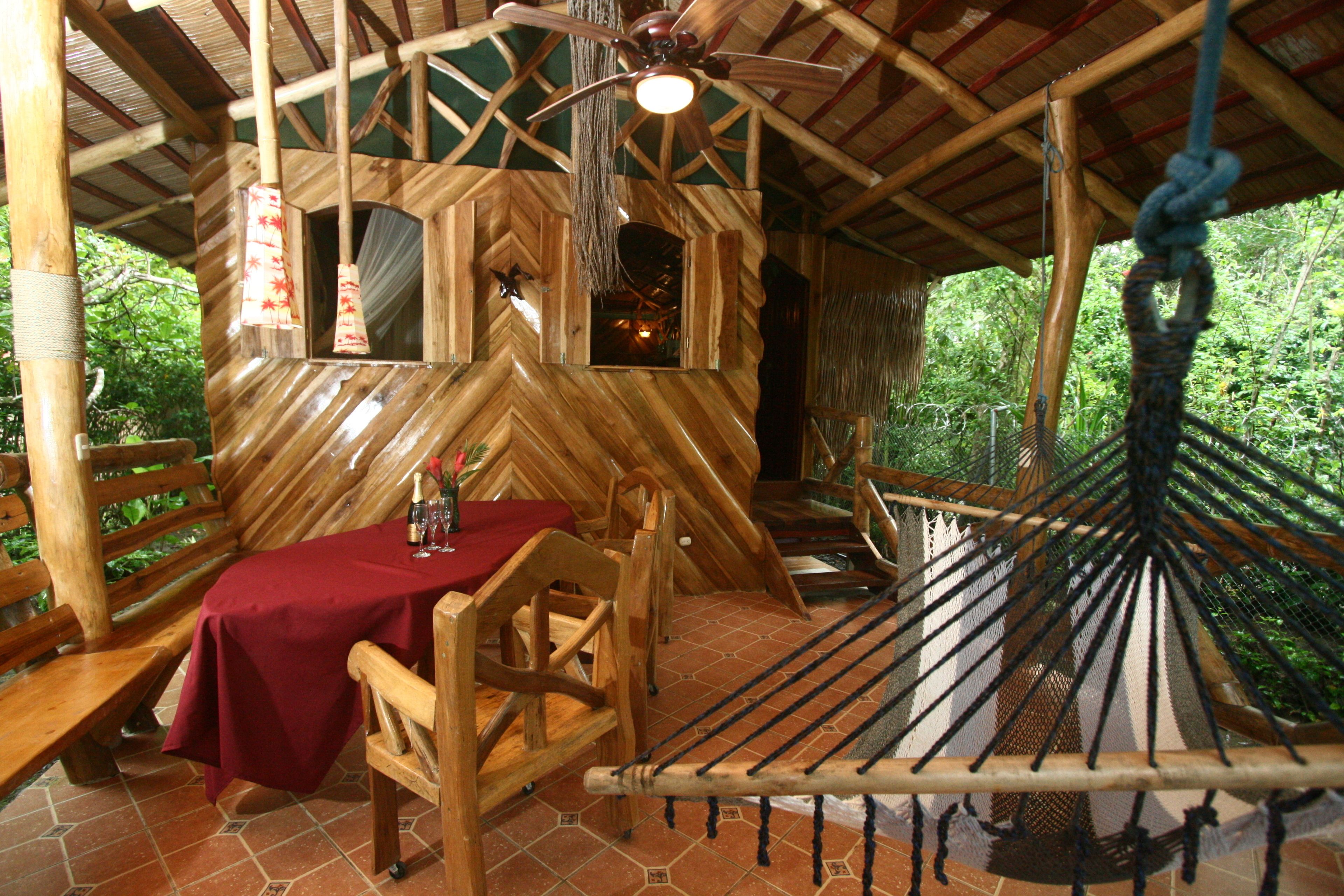 Una cabaña de madera con una mesa preparada para dos, una hamaca y un ventilador de techo.
