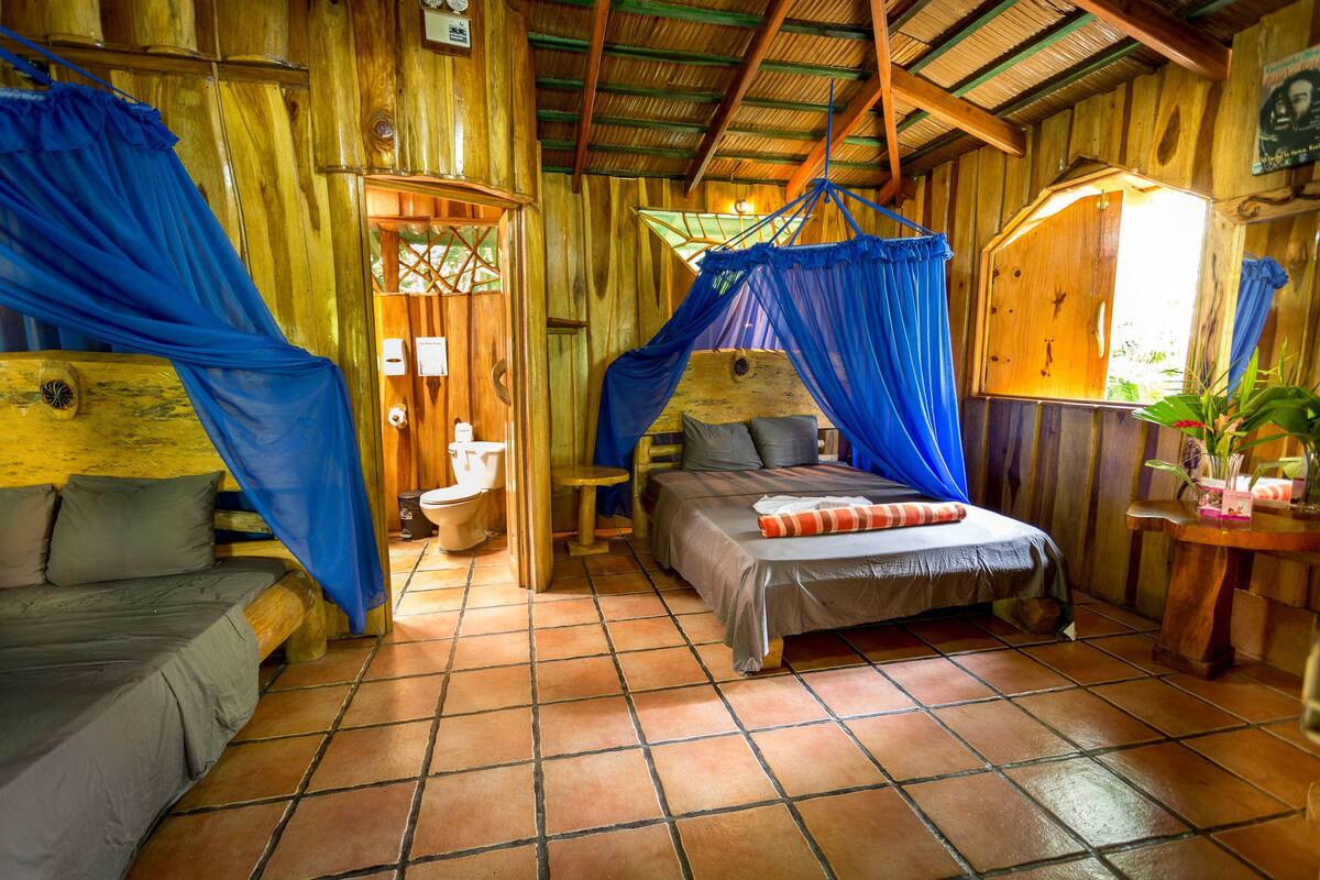 Una habitación rústica de madera con una cama, una mesita pequeña y un banco.