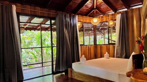 A room with a bed, a small table, and a window with curtains. - La Costa de Papito (Cahuita)