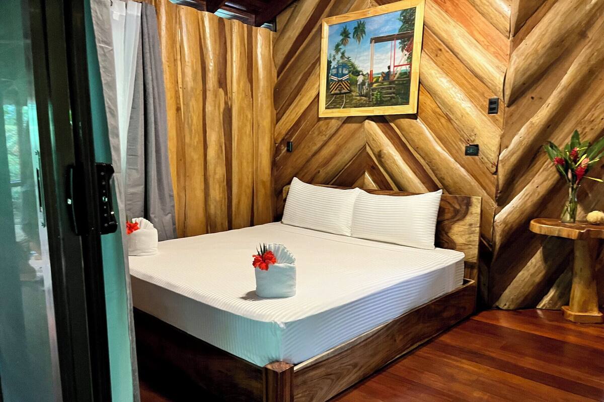 Una habitación con paneles de madera, una cama, un cuadro y una pequeña mesa con flores.