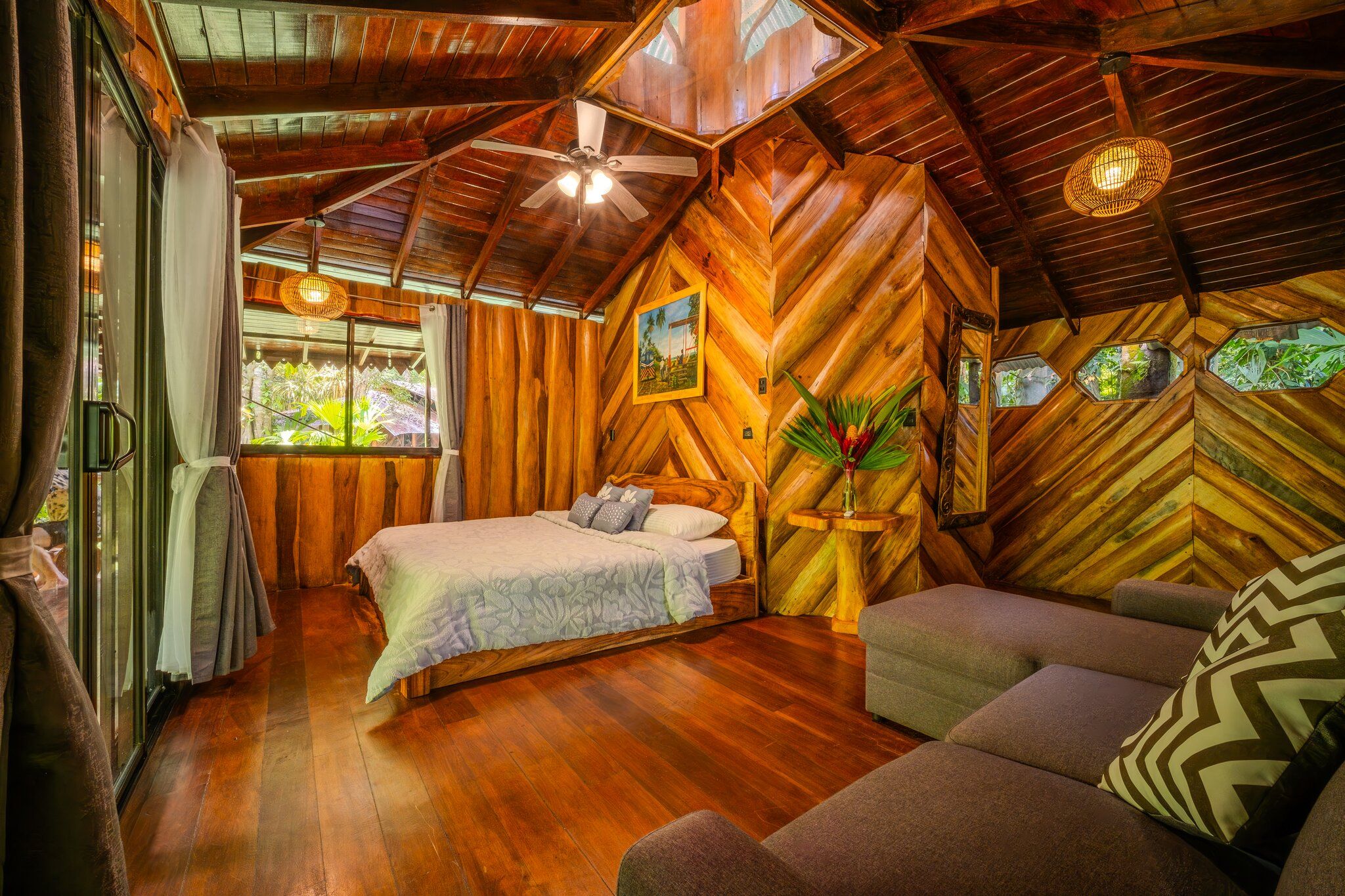 A wooden interior with a bed, a sofa, and a ceiling fan.